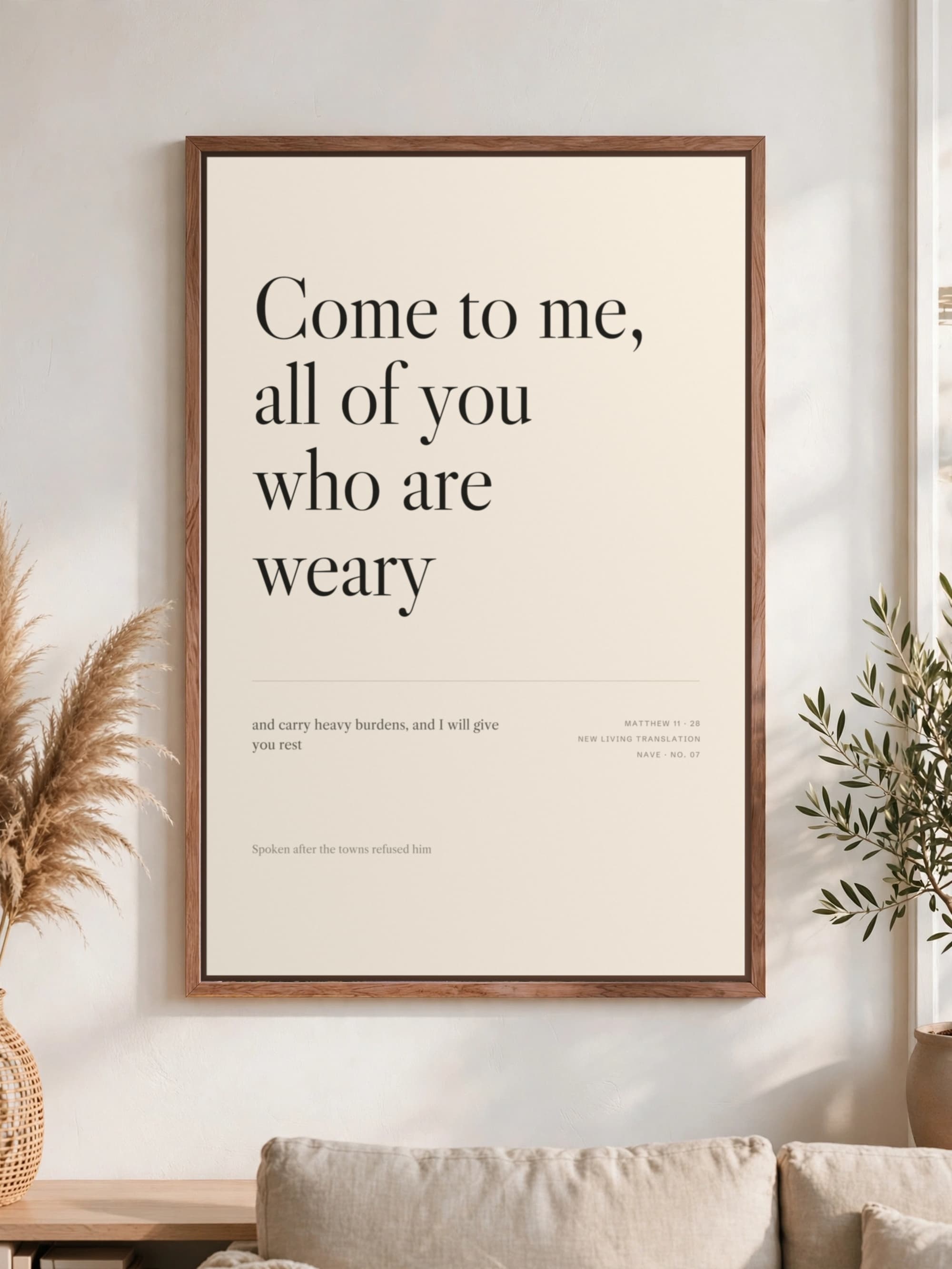 “Come to me, all of you who are weary” in dark serif on cream canvas, pecan frame, hung above a linen sofa.