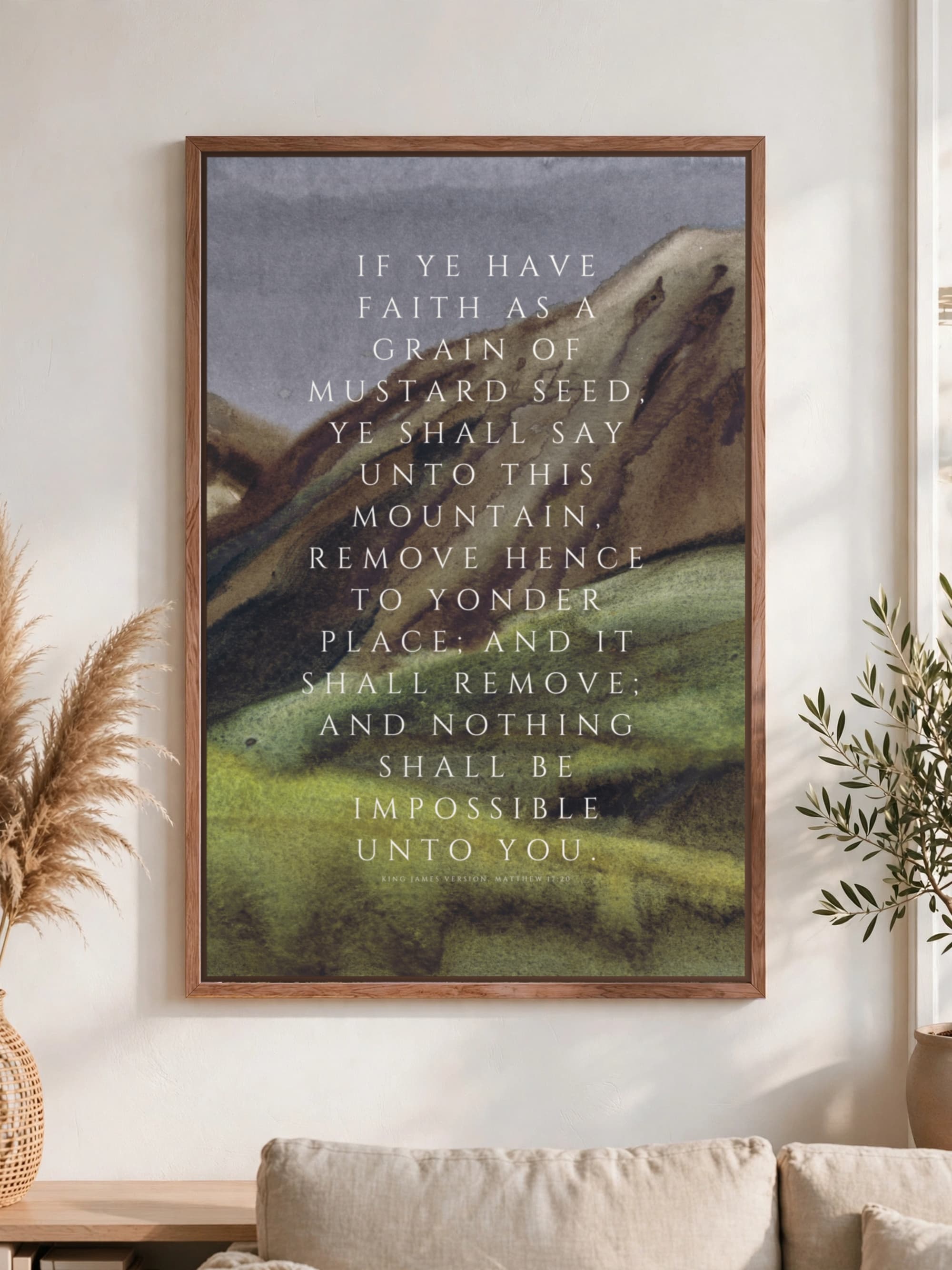 Matthew 17:20 in spaced white capitals over a painted green hillside, pecan frame, hung above a linen sofa.